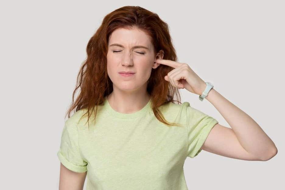 Headshot of a woman suffering from Tinnitus, isolated over a gray background.